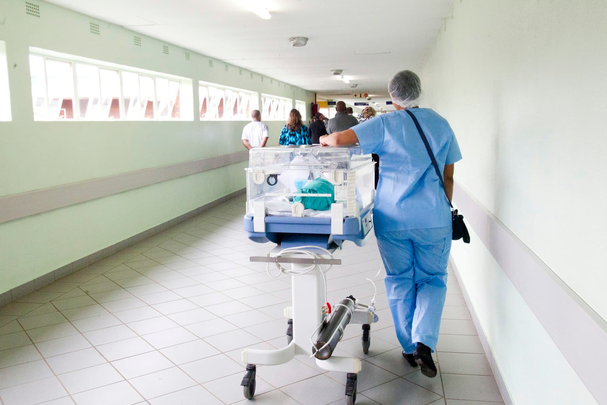 Nurse pushing an incubator along a hospital corridor